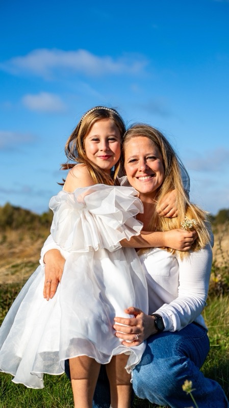 Mama knuffelt haar dochter in een wit kleedje, buitenshoot