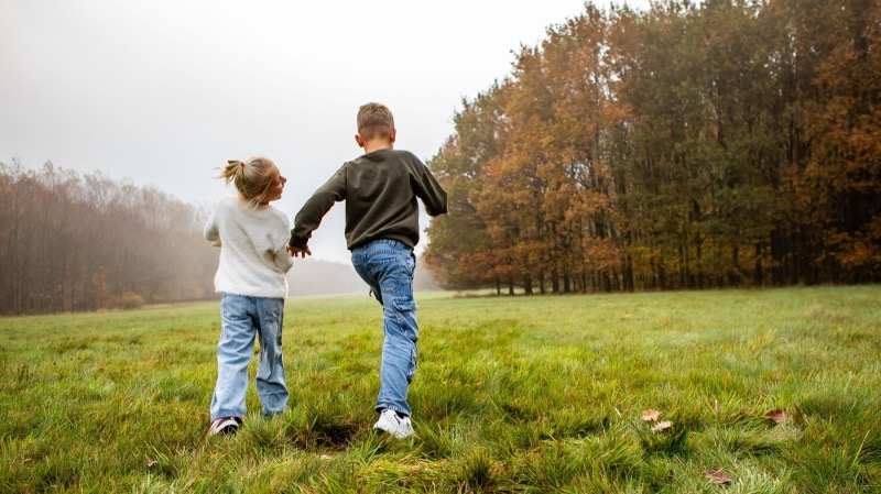 Twee kinderen lopen hand in hand over een grasveld