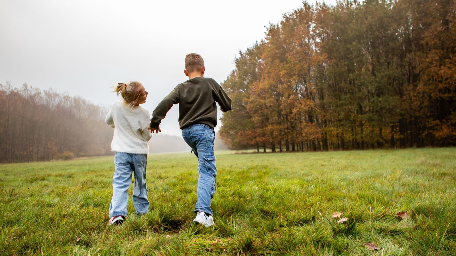 Twee kinderen lopen hand in hand over een grasveld