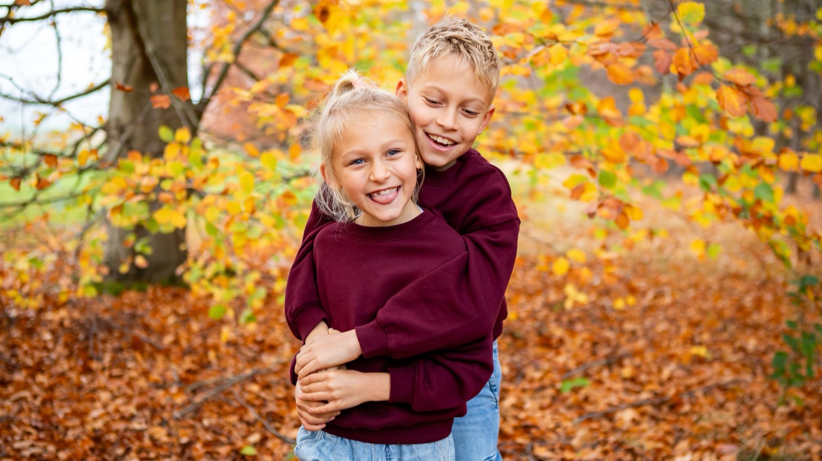 Broer en zus knuffelen tussen de gele herfstbladeren