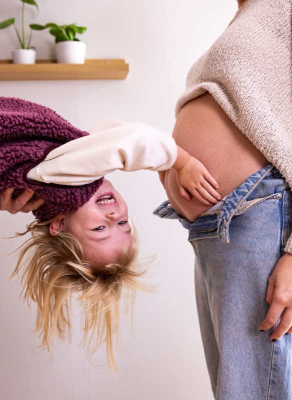 Dochtertje kijkt ondersteboven naar de buik van mama