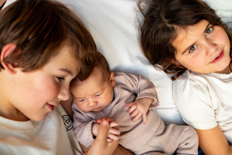 Broer en zus liggen naast de pasgeboren baby