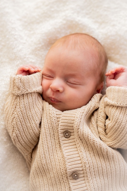 Slapende newborn baby in een beige gebreid vestje