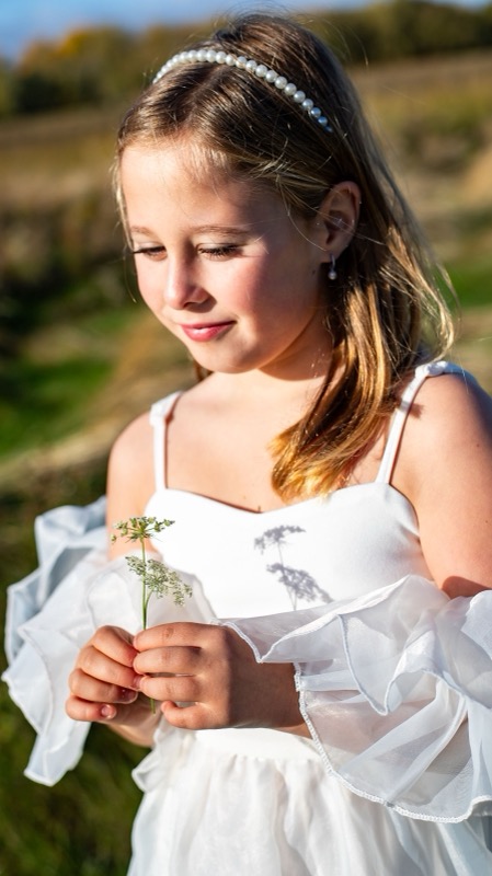 Meisje in een wit kleedje met een bloemetje in het gouden licht